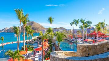 Un área de piscina en un resort con varias piscinas, palmeras y vistas a la playa.