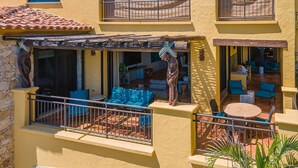 A balcony with blue furniture, a stone wall, and a tiled roof. - Newly Renovated Condo With Ocean View Luxury Amenities in Beachfront Resort Walk to Downtown (Cabo San Lucas)