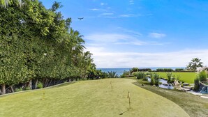 Ein Golfplatz mit freiem Blick auf den Ozean, umgeben von üppiger Vegetation und Palmen.