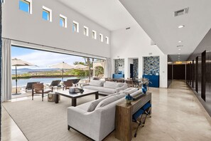 A spacious living area with a large window overlooking a scenic landscape, a modern kitchen, and a hallway leading to a darkened room. - Breathtaking Villa Boasting a Private Putt Chip Course Gym Tennis Court Resort Access More (San José del Cabo)