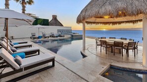 An infinity pool with lounge chairs and a dining area overlooking the sea. - Ultra Exclusive Beachfront Villa Just Steps From the Sand Butler Included (San José del Cabo)