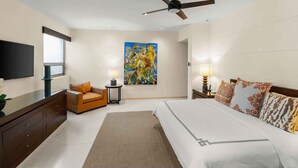 Habitación de hotel con cama, sofá, televisión, un cuadro y ventilador de techo.