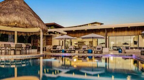 A pool area with lounge chairs and umbrellas, a thatched structure, and a modern building with large windows. - Ultra Exclusive Beachfront Villa Just Steps From the Sand Butler Included (San José del Cabo)