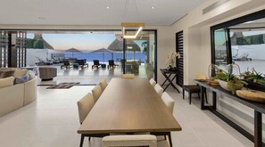 A modern dining area with a long table, chairs, and a view of the ocean. - Ultra Exclusive Beachfront Villa Just Steps From the Sand Butler Included (San José del Cabo)