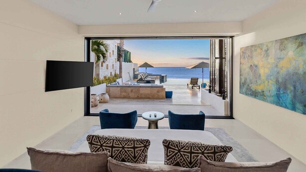 Una habitación de hotel moderna con un ventanal grande, un televisor de pantalla plana, un comedor con mesa y sillas, y vistas al mar.