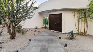 Un edificio curvo con una puerta oscura, rodeado por un camino de grava y diversas plantas.