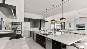 A modern kitchen with a large island, stainless steel appliances, and pendant lighting. - Brand New Villa BIG Ocean View Gym Close to the Beach (San José del Cabo)