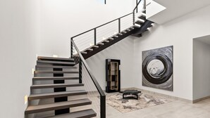 A modern staircase with a glass railing, a large abstract painting, and a minimalist coffee table. - Brand New Villa BIG Ocean View Gym Close to the Beach (San José del Cabo)