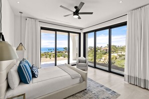 Ein modernes Schlafzimmer mit einem großen Bett, einem Deckenventilator und Blick aufs Meer.