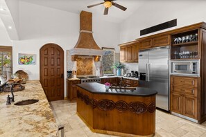 A kitchen with a central island, stainless steel appliances, wooden cabinets, and a decorative ceiling fan. - Ultra Private Villa w Open Floor Plan Premium Bedding Big Ocean View Daily Butler Included (San José del Cabo)