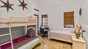 Een kamer met stapelbedden, een bureau, een stoel, een raam met zonwering en decoratieve sterren aan de muur.