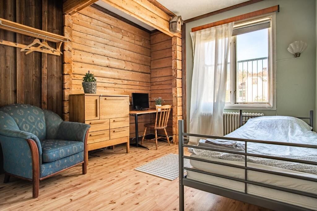 A log cabin room with a bed, a desk, a chair, and a hanging coat rack.