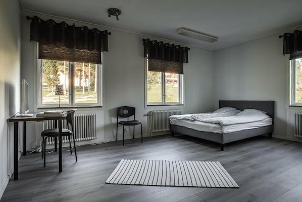 Une chambre à coucher avec un lit, un bureau, une chaise et deux fenêtres avec des rideaux.