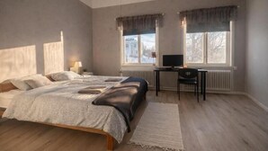 A bedroom with a bed, a desk, a chair, and two windows with curtains. - Wärdshuset Liden (Liden)