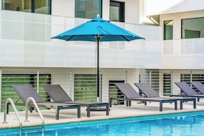 A poolside area with lounge chairs and a blue umbrella. - Eco-Friendly Condo with Shared Seasonal Pool, Balcony, and Free WiFi (Nashville)