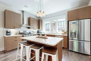 A modern kitchen with wooden cabinets, a stainless steel refrigerator, and a central island with stools. - Modern Townhome, Open Living Space, Near Nashville (Nashville)