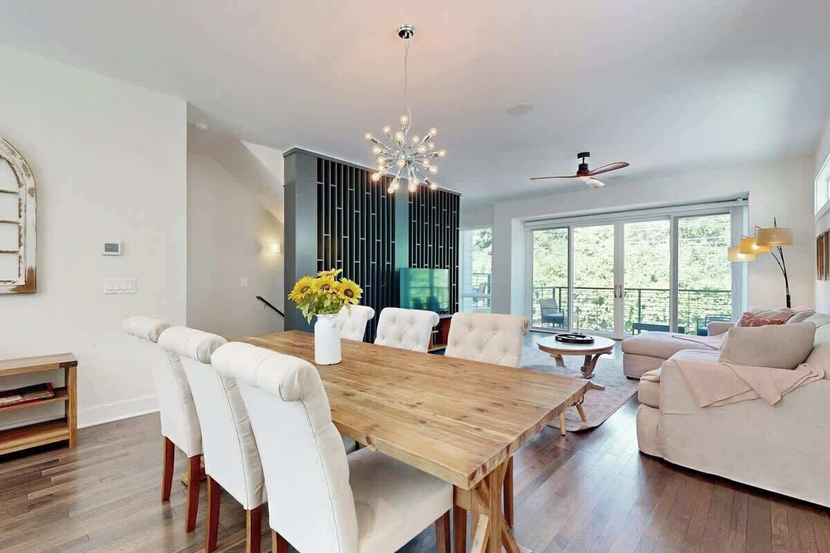 A modern living room with a wooden dining table, white upholstered chairs, a sofa, and a ceiling fan.