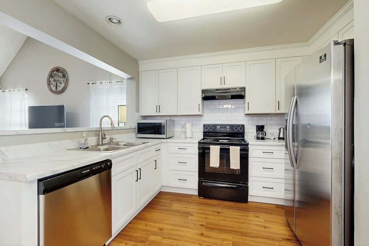 A kitchen with white cabinets, a stainless steel dishwasher, a black oven, a microwave, and a refrigerator.