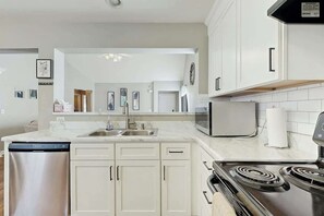 Een moderne keuken met witte kasten, een roestvrijstalen vaatwasser, een magnetron en een fornuis.