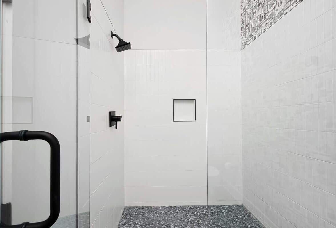 A modern shower with a glass door, a black showerhead, and a small square mirror.
