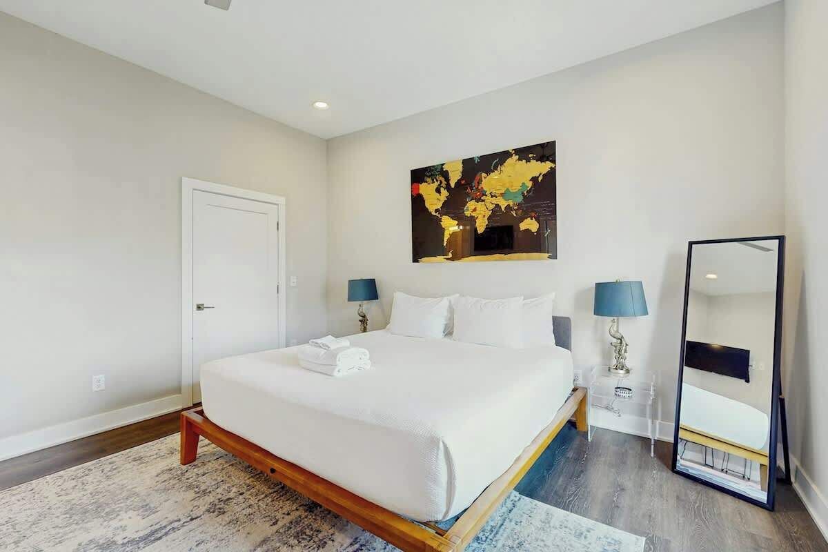 Een hotelkamer met een groot bed, twee nachtkastjes met lampen, een wereldkaart als kunstwerk, een spiegel en een deur.