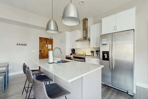 A modern kitchen with a central island, stainless steel appliances, pendant lighting, and a dining area with chairs. - Downtown West End Nashville Retreat, Near Broadway (Nashville)