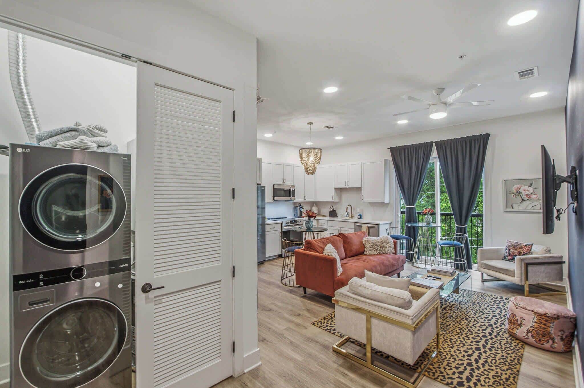 A modern apartment with a laundry area, a kitchen, a living room with a sofa and chairs, and a dining area.
