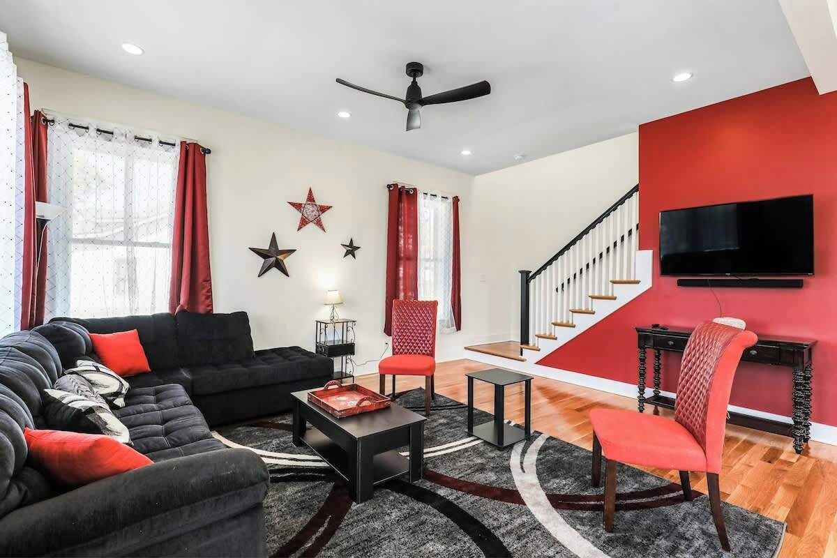 Un salon avec un canapé noir, des fauteuils rouges et noirs, une table basse et un escalier avec un mur rouge.