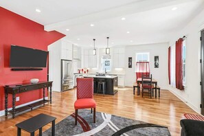 A modern living room with a red accent wall, a flat-screen TV, a dining area with a red chair, and a kitchen with a bar. - 4BR Music City Escape Near Broadway, Sleeps 10 (Nashville)