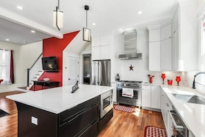 A modern kitchen with white cabinets, a stainless steel refrigerator, and a red accent wall. - 4BR Music City Escape Near Broadway, Sleeps 10 (Nashville)