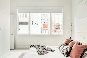 A bedroom with a large window, a bed with pillows, and a blanket on the floor. - Charming condo with central AC, full kitchen, & tasteful decor (Nashville)