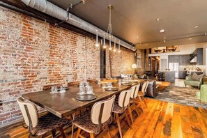 Un comedor con pared de ladrillo, suelo de madera y una mesa larga dispuesta para seis personas.
