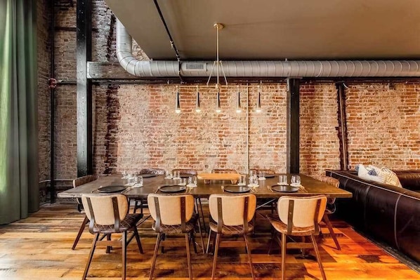 A dining area with a brick wall, exposed ductwork, a wooden floor, and a black leather couch.