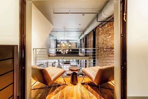 A modern interior with a wooden floor, two leather chairs, a small round table, and a brick wall.