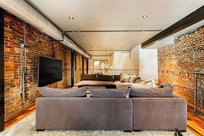 A modern living room with a large sectional sofa, a flat-screen TV, and exposed brick walls.