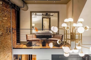 A loft-style bedroom with a loft bed, a modern chandelier, and exposed brick walls.