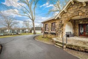 A stone building with a curved driveway, a bench, and a tree-lined street. - Historic East Nashville Cottage Shared Pool Gym (Nashville)