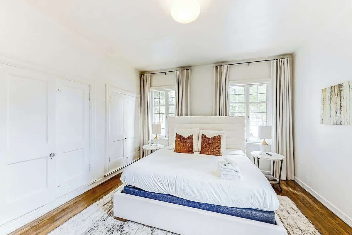 A bedroom with a large bed, two bedside tables, a window with curtains, and a door.