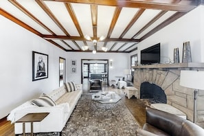 A living room with a fireplace, a sofa, a coffee table, and a television. - Historic East Nashville Cottage Shared Pool Gym (Nashville)