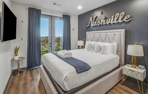 A hotel room with a large bed, a balcony with curtains, a wall-mounted TV, and a sign that reads 'Nashville'. - Rockstar Downtown Condo Escape & Private Balcony (Nashville)