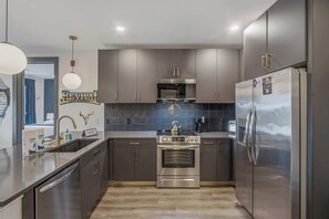 A modern kitchen with stainless steel appliances, grey cabinetry, and a tiled backsplash. - Rockstar Downtown Condo Escape & Private Balcony (Nashville)