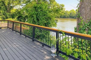 Eine Holterrasse mit schwarzer Geländer, mit Blick auf einen Fluss und üppiges Grün.