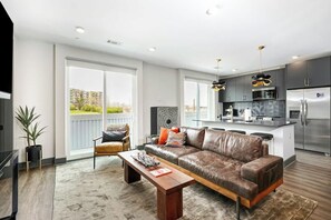 A modern living room with a leather sofa, a wooden coffee table, and a large window. - Second-floor Condo with High-speed WiFi & Balcony (Nashville)