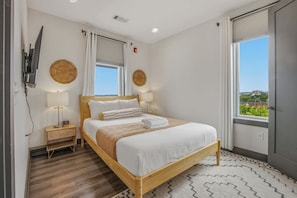 Quarto de hotel com cama, mesas de cabeceira, televisão e vista para a cidade.
