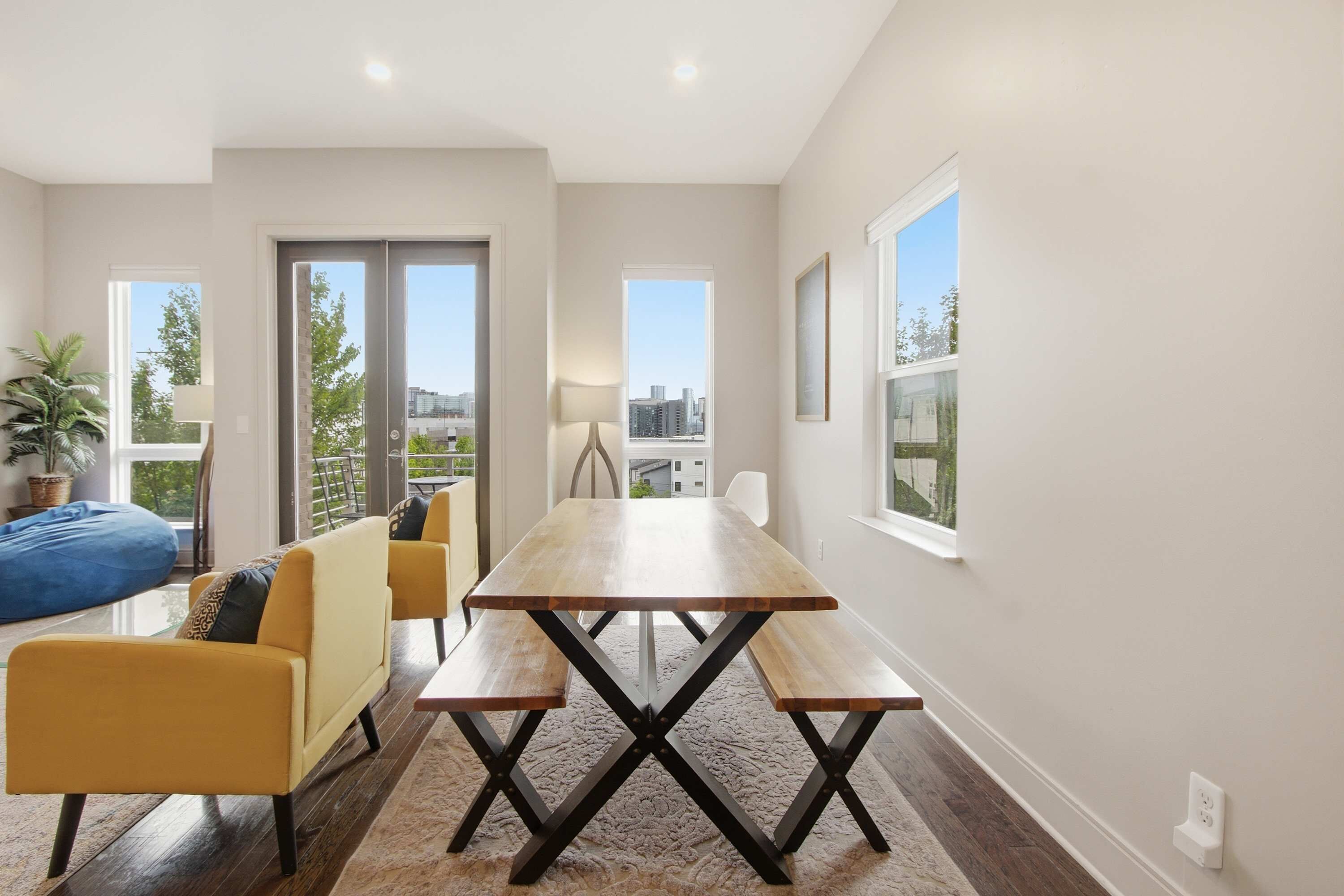 A modern dining area with a wooden table and benches, a sofa, and a view of the city.