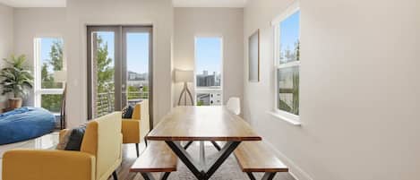 A modern dining area with a wooden table and benches, a sofa, and a view of the city.