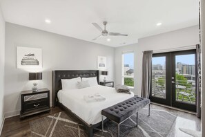 A modern bedroom with a large bed, a bench, a ceiling fan, and a view of the city through a large window. - 1 mi to Music Row The Gulch Rooftop Deck W Views (Nashville)