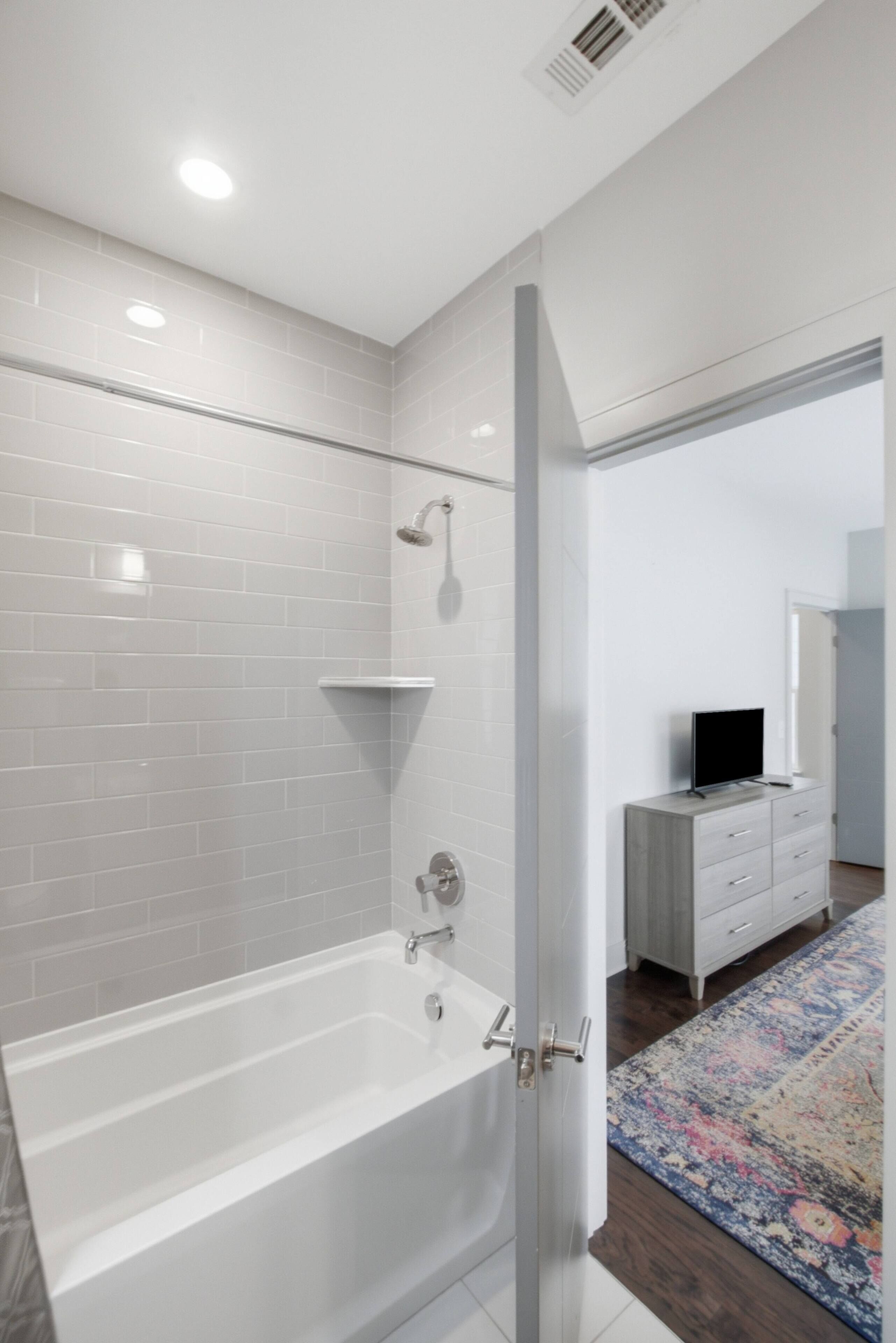 Une salle de bain moderne avec une baignoire blanche, une douche et une porte en verre donnant sur une chambre.