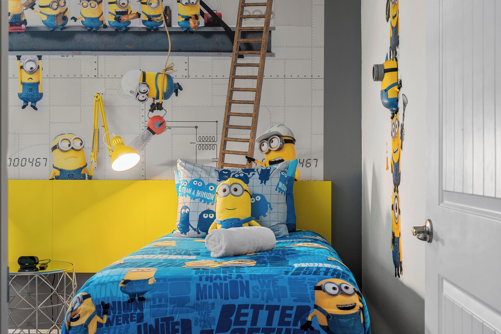 Ett rum med en säng med sängkläder med Minion-motiv, en stege och dekorationer på väggarna.