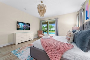 Ein Schlafzimmer mit Bett, Fernseher, Schminktisch, Stuhl und Blick auf einen Pool.
